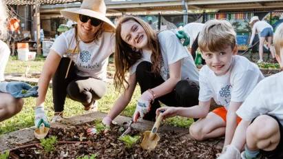 A group of children hold trowels and other gardening tools, generously volunteering their time to do good through their local church.