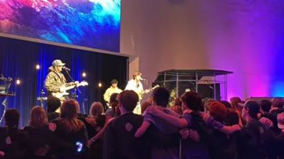 A sea of students sing with their arms around each other while watching the band perform on the stage at the St. Luke's United Methodist Church in Houston, Texas.