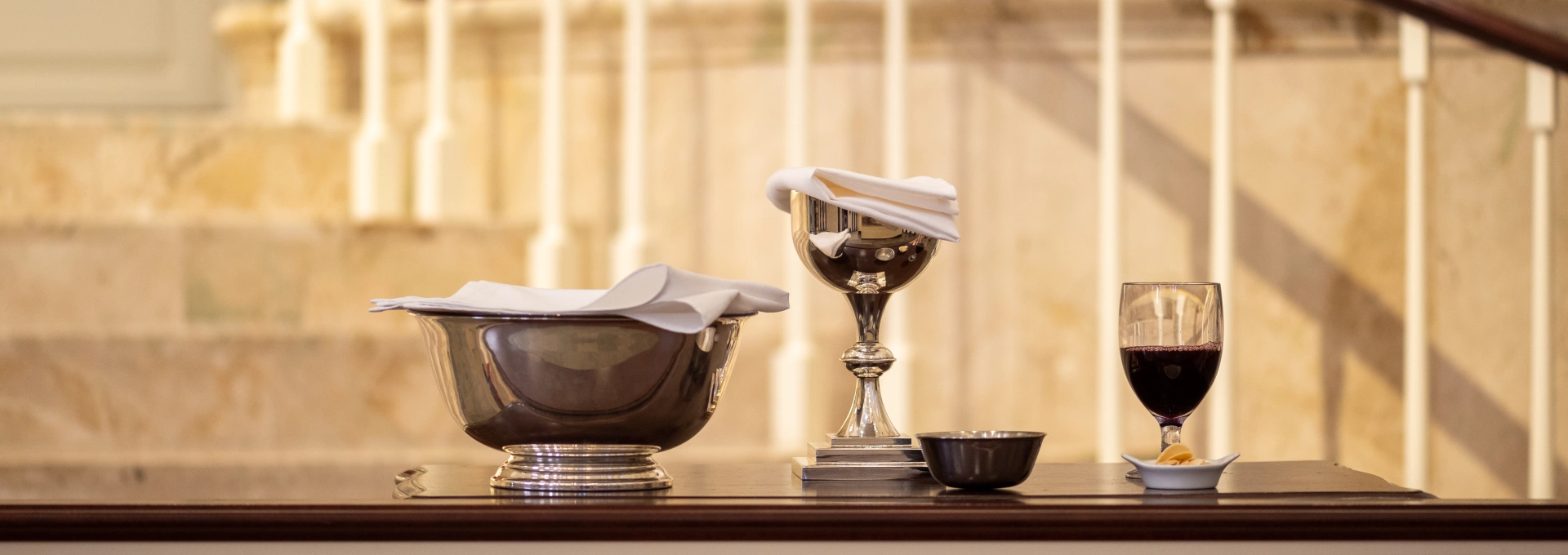 A bowl, a chalice, and a wine glass, ready to serve communion, sit on a table in front of the steps of St. Luke's Sanctuary stage.
