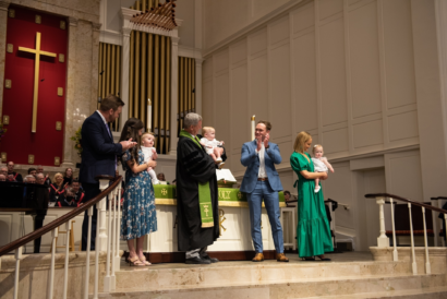 Two families stand next to Dr. Tom Pace while he performs the rite of baptism in St. Luke's Sanctuary for their three happy children.