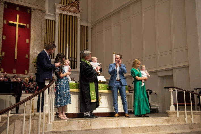 Two families stand next to Dr. Tom Pace while he performs the rite of baptism in St. Luke's Sanctuary for their three happy children.